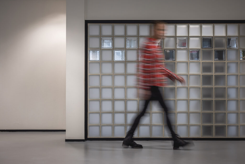 Dynamische actiefoto van een medewerker die langs een glazen wand loopt op het kantoor van Factor Werkt.